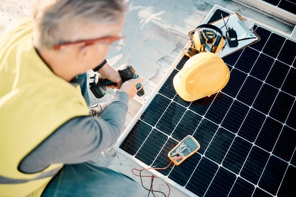 Solar energy, industrial work and senior construction worker on a building roof with panel. Sustainability, electricity and industrial grid with a mature engineer drilling with tools outdoor.