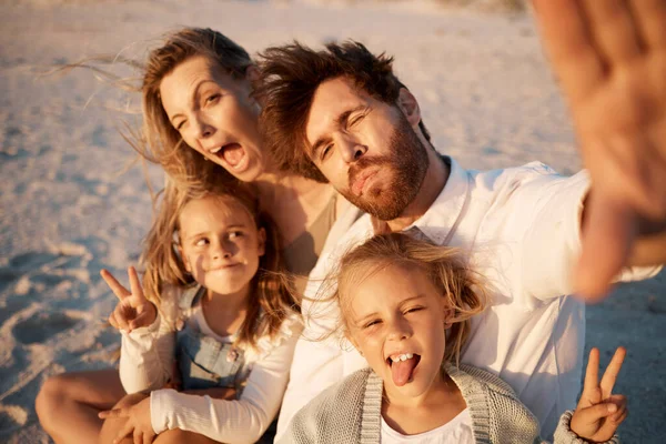 Family having fun taking a selfie on the beach. carefree family making silly faces in a selfie. Happy father taking a photo with his family. Little girls having fun with their parents by the ocean.