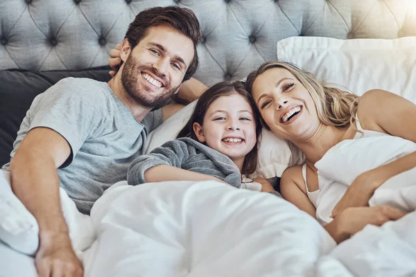 Love, family and portrait in home bedroom, laughing at funny joke and bonding together. Care, comic and happy man, woman and girl, child or kid in bed, having fun and enjoying quality time in house