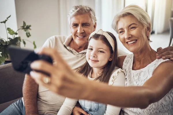Selfie, smile or happy grandparents with girl in living room bonding as a family in Australia with love. Pictures, senior or elderly man relaxing with old woman or child at home together on holiday.