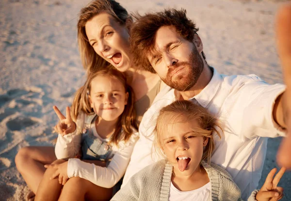 Family taking a selfie on the beach. Carefree family enjoying a holiday by the beach. Happy family taking a photo during vacation on the beach. Parents enjoying a holiday with their little children.