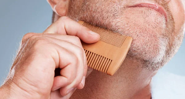 Grooming, hair care and man brush beard for wellness, healthy skin and hygiene on blue background. Salon aesthetic, cleaning and face zoom of male with barber comb for facial, skincare and beauty.