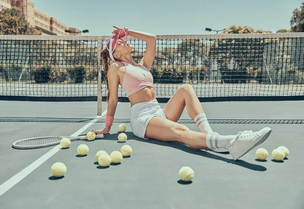 Fashion, tennis and woman model on the court posing with a racket and balls before a game. Sports, fitness and female athlete sitting at an outdoor stadium before a match, training or practice