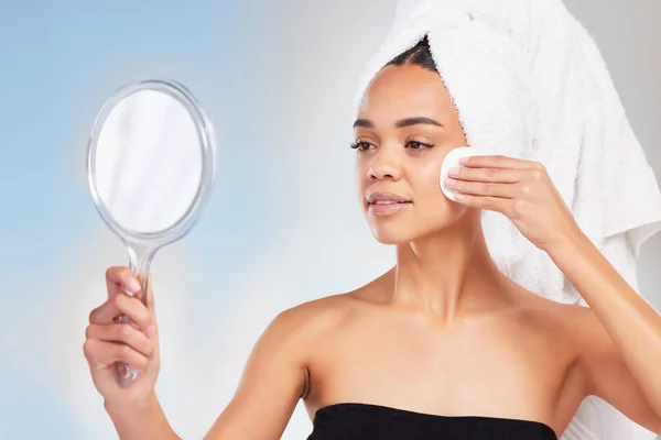 Doing skincare the right way. a young woman looking in a mirror against a blue background