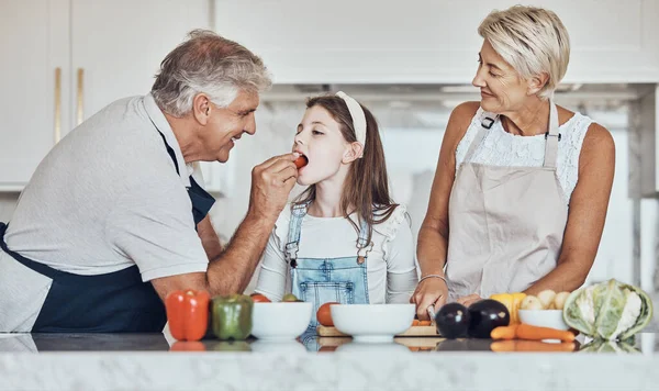 Love, grandparents or girl cooking or eating as a happy family in house kitchen with organic vegetables for dinner. Grandmother, old man or young child bonding or helping with healthy vegan food diet.