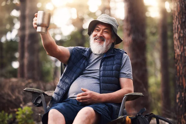 Camping, old man and in forest with coffee, smile and fresh air with break, vacation and relax. Camper, mature male and elderly guy with mug, tea and in woods for hobby, happiness and active citizen.