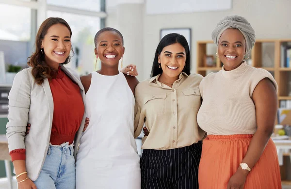 Portrait of a diverse group of smiling ethnic business women standing together in the office. Ambitious happy confident professional team of colleagues embracing while feeling supported and empowered.