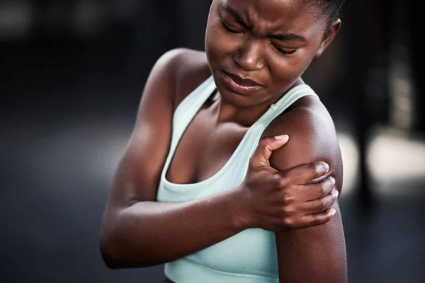My shoulder hurts. a young woman holding her shoulder in pain while at the gym