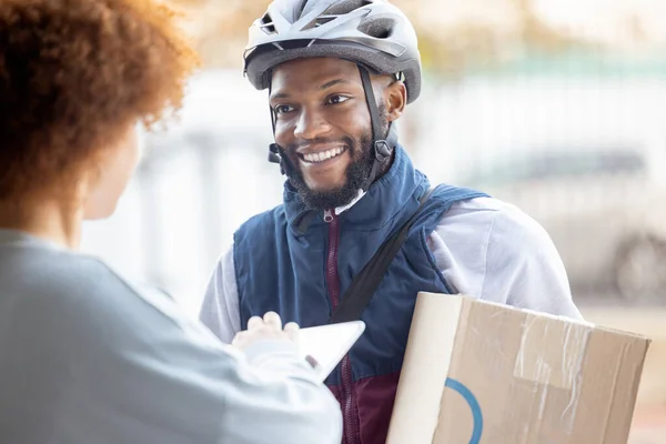Black man, box and smile for delivery service, package or female customer order in city. Happy African American male courier employee smiling or delivering cargo to woman with clipboard for signature.