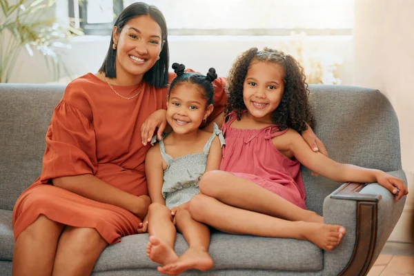 A happy mixed race family of three relaxing in the lounge and sitting on the couch together. Loving black single parent bonding with her daughters while relaxing on a sofa at home.