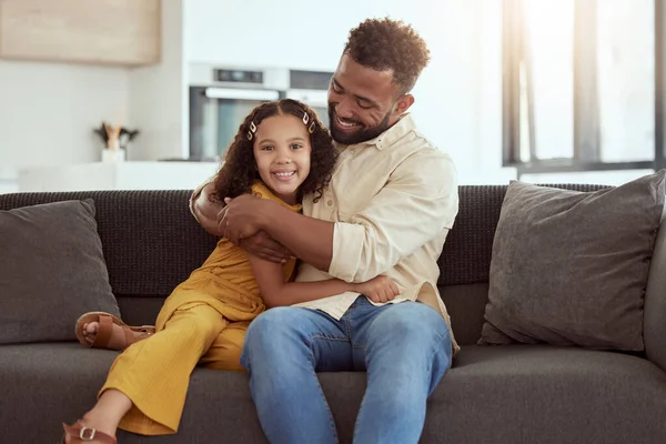 Portrait of mixed race single father and daughter hugging in home living room. Smiling hispanic girl embracing and bonding with single parent in lounge. Happy man and child sitting together on weeken.
