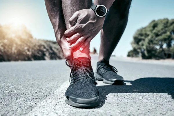 Closeup fit mixed race man holding his ankle in pain while exercising outdoors. Unrecognizable male athlete suffering with a joint injury highlighted by glowing cgi. You can get hurt during a workout.