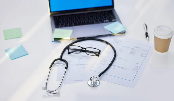 Laptop, stethoscope and medical paperwork in a office for research, diagnosis or test results. Sticky notes, coffee and glasses on a desk for doctor to read healthcare documents in hospital or clinic.