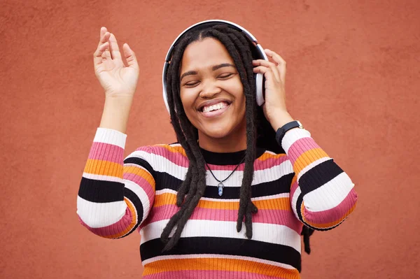 Black woman, music headphones and wall with smile in city for walk, adventure and listening to edm on radio. Young gen z girl, streaming hip hop or techno on website, internet and happiness in metro.
