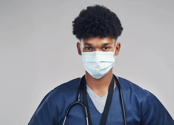 Not all heroes wear capes, some wear masks. a male nurse wearing a surgical mask while standing against a grey background