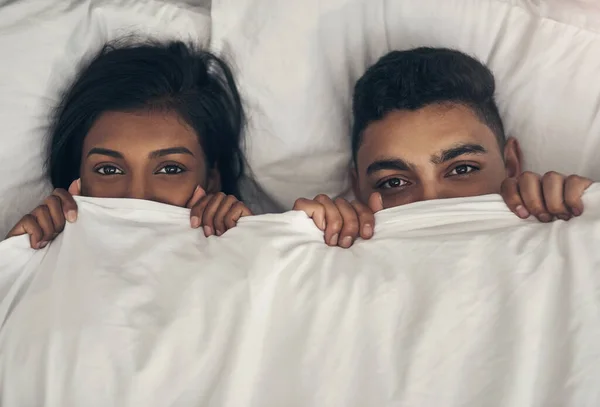 Staying under covers sounds like a good plan today. Portrait of a playful young couple hiding under the covers in a bed