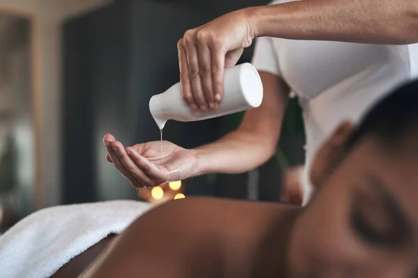 This soothing massage oil will work wonders. Closeup shot of a massage therapist pouring body oil into her hands while giving a massage to a customer at a spa