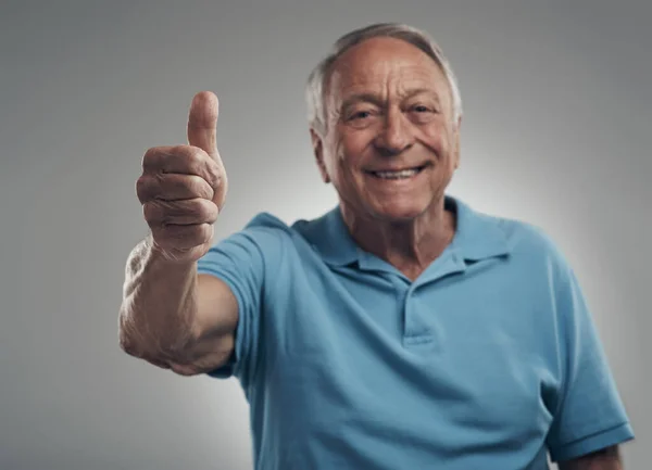 Id do this day all over again happily. a happy elderly man giving the thumbs up in a studio against a grey background