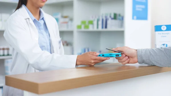 Patient buying medicine from pharmacist at the pharmacy store. Customer receives prescription medication at the chemist store from medical doctor. Healthcare professional accepts credit card payment.