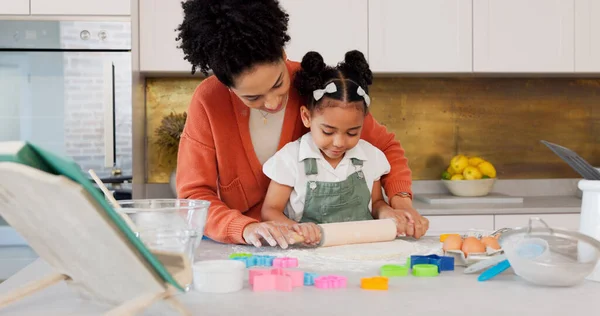 Mother, girl learning baking in kitchen and rolling flower dough on counter to cook cookies for fun, learning and development. Happy mom, black child with smile and teaching daughter to bake together.