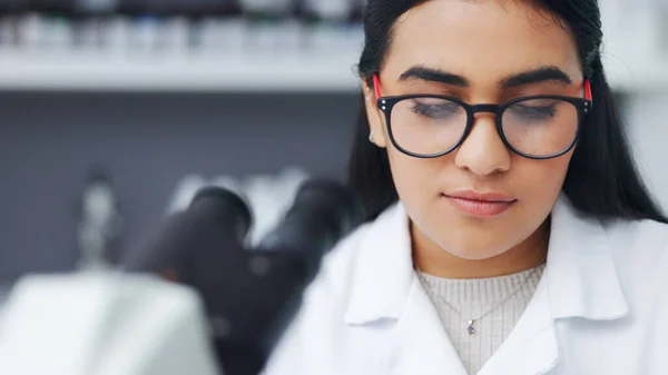 Closeup of a young female scientist using a microscope analysing medical test results or samples in a research lab. Young woman doing forensic science and experiment to develop or discover a cure.