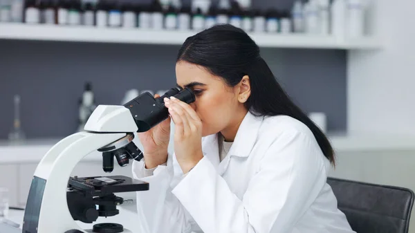 Female scientist using a microscope in a research lab. Young biologist or biotechnology researcher working and analyzing microscopic samples with the latest laboratory tech equipment.