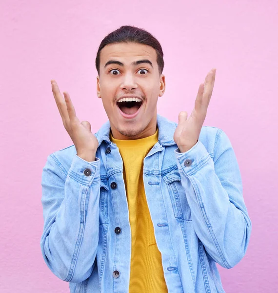 Man, hands and face for surprise in portrait with happiness, excited and pink wall background. Happy gen z model, wow and smile for announcement, fashion and news for career, success and life goal.