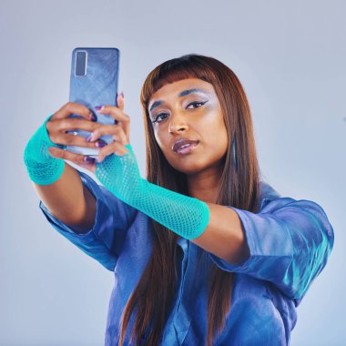 Moda, selfie ve akıllı telefonlu kadın ve mavi arka planda izole edilmiş siberpunk neon giysiler. Sosyal medya, gelecek ve modaya uygun z etkileyicisi profil fotoğrafı için stüdyoda telefonla Hindistan 'dan.