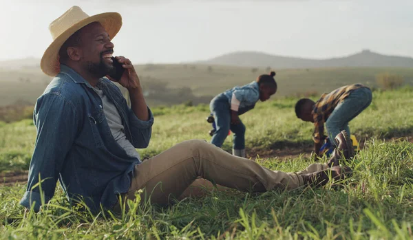 Families who farm together stay together. a mature man using a smartphone while son and daughter play in the soil on a farm