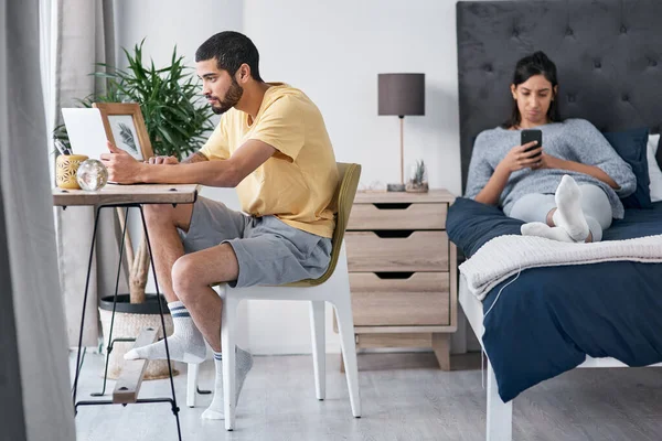 Personal and professional life co-existing in perfect harmony. a young man working from home while his wife uses a smartphone on the bed