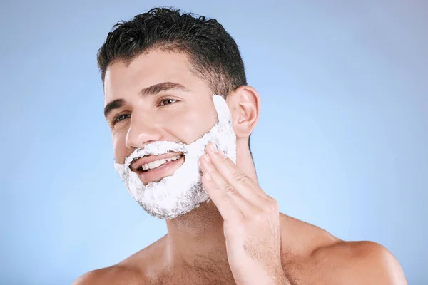 Shaving, foam on beard and man with smile and hand on face, product placement and mock up in studio. Shave cream, hair and skincare for happy male model facial grooming, isolated on blue background