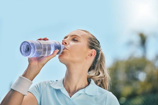 Woman, tennis player and drinking water for hydration after workout, exercise or intense training in nature. Sporty female with bottle for refreshing drink to stay hydrated during sports exercising.