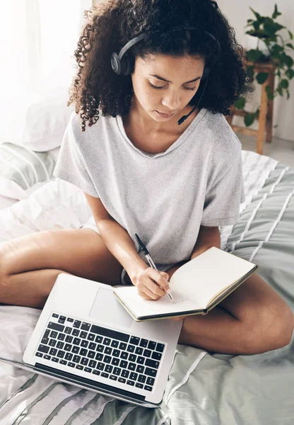 Book, writing and black woman with laptop and headphones for studying or online learning. Scholarship, student and female with headset, computer and notebook in virtual class on bed in bedroom home