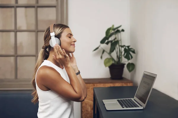 What will be the soundtrack of your success story. a young businesswoman using headphones and a laptop in a modern office