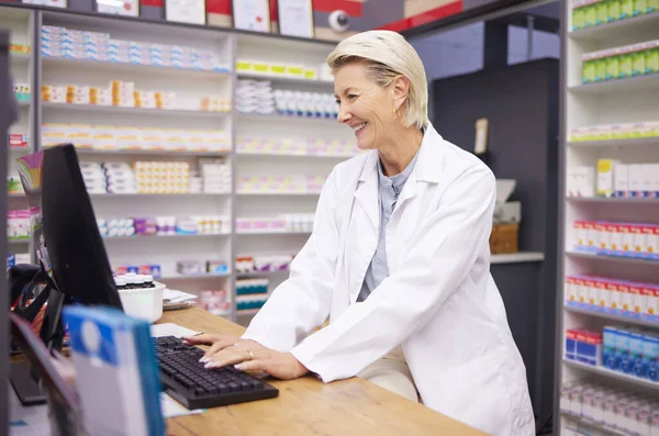 Pharmacy, computer database and senior woman pharmacist working of medicine research. Pharmaceutical data, typing and healthcare employee smile checking online information for medical prescription.