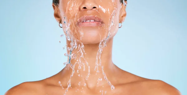 Face, water and cleaning with a black woman in studio on a blue background for hygiene or hydration. Splash, shower and bathroom with a young female washing her body for natural skincare or wellness.
