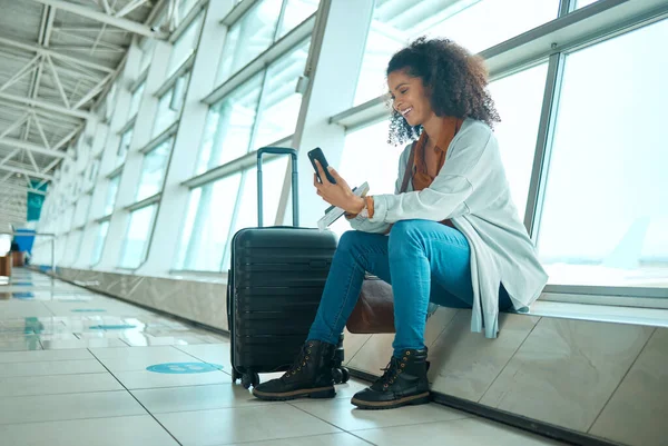 Travel, phone and black woman at airport on a video call waiting for plane travel and flight. Online, mobile connection and smile of a young female sitting at airplane terminal waiting for transport.