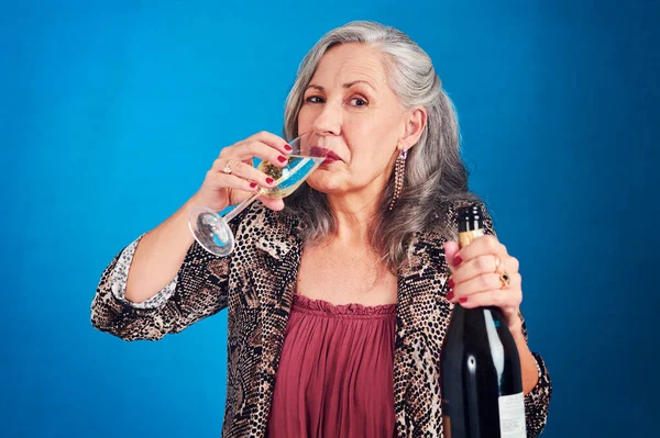 Good times start with a glass of champagne. Portrait of a funky and cheerful senior woman drinking champagne in studio against a blue background