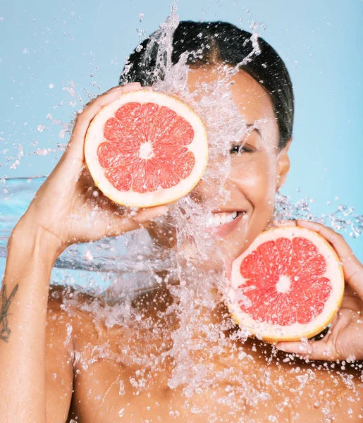 Water splash, skin care and woman with a grapefruit for healthy skin and diet on blue background. Face of aesthetic model person with beauty smile and fruit for sustainable facial health and wellness.