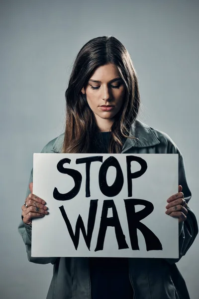 War, stop and sad woman with a sign as a voice isolated on a grey studio background. Protest, crime and girl with a board against conflict, violence and danger with an opinion in Russia on a backdrop.