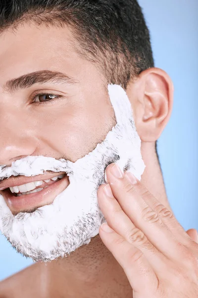 Shaving, foam and smile on face, man with hand on beard, product placement and mock up in studio. Shave cream facial, luxury hair and skincare for male model with smile, isolated on blue background