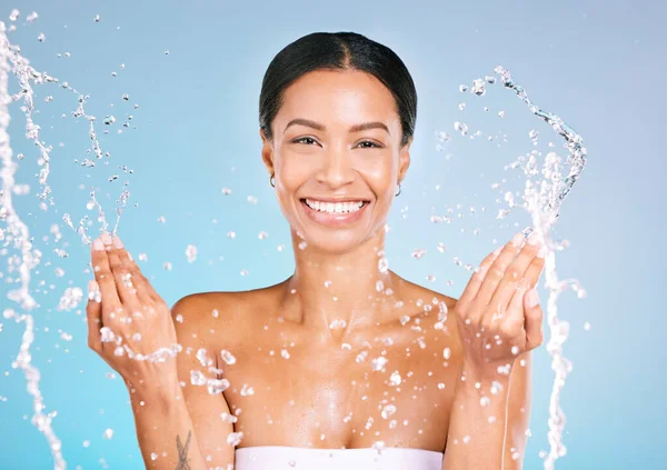 Portrait, black woman and water for cleaning, dermatology and smile with wellness, health and blue studio background. Face detox, African American female and happy lady with liquid, aqua and skincare.
