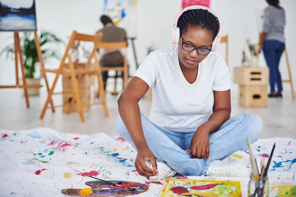 Music is what gets the creative juices flowing. a young woman wearing headphones while painting in a art studio