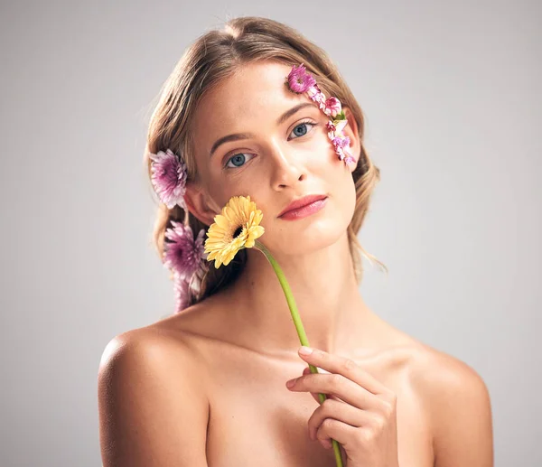 Skincare, flower and portrait of model in studio with beauty, natural and face routine. Floral, health and woman with organic, self care and fresh skin or facial treatment isolated by gray background.