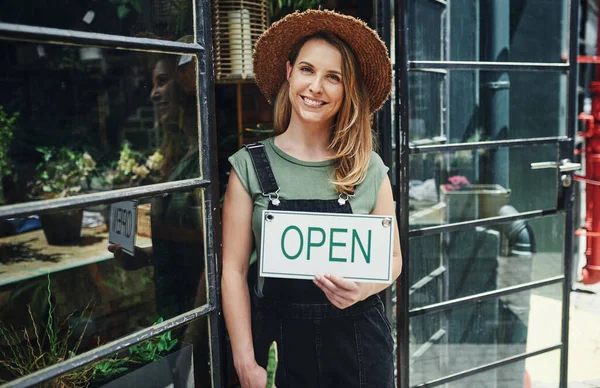 I finally opened my flower store. Cropped portrait of an attractive young business owner standing alone and holding the open sign at the floristry entrance