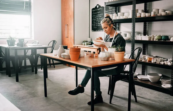 Deep in thought. Full length shot of an attractive mature woman sitting alone and painting a pottery bowl in her studio