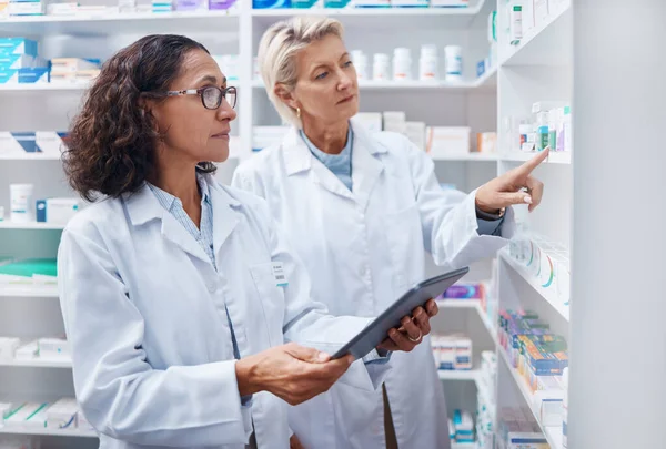 Tablet, teamwork and pharmacists check stock in pharmacy, drugstore or shop for medication. Medicine, technology and medical doctors or senior women with touchscreen for checking product inventory