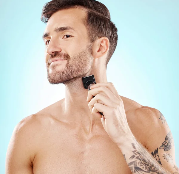 Man, beard and shaving with trimmer in studio isolated on a blue background for hair removal. Haircare thinking, grooming and male model with electric shaver to shave for hygiene, health or wellness