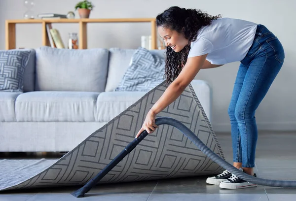 Woman, vacuum and cleaning carpet floor in housekeeping for clean sanitary hygiene at home. Happy female cleaner in germ or dust removal in living room interior by sofa for daily chores or routine.
