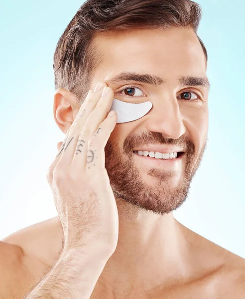 Skincare, face and man with eye patch in studio isolated on a blue background. Beauty, portrait and male model with pad product for dermatology, cosmetics and facial treatment, wellness and health